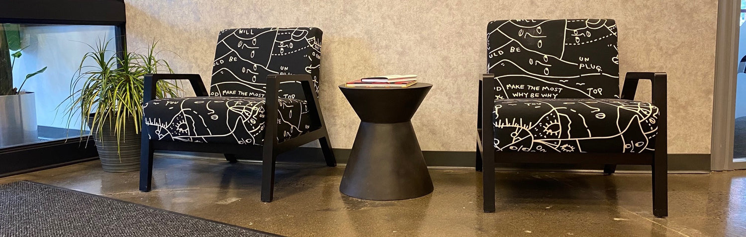Two accent chairs with a black fabric featuring a white pattern of hand-drawn faces. Gray accent table between the chairs.